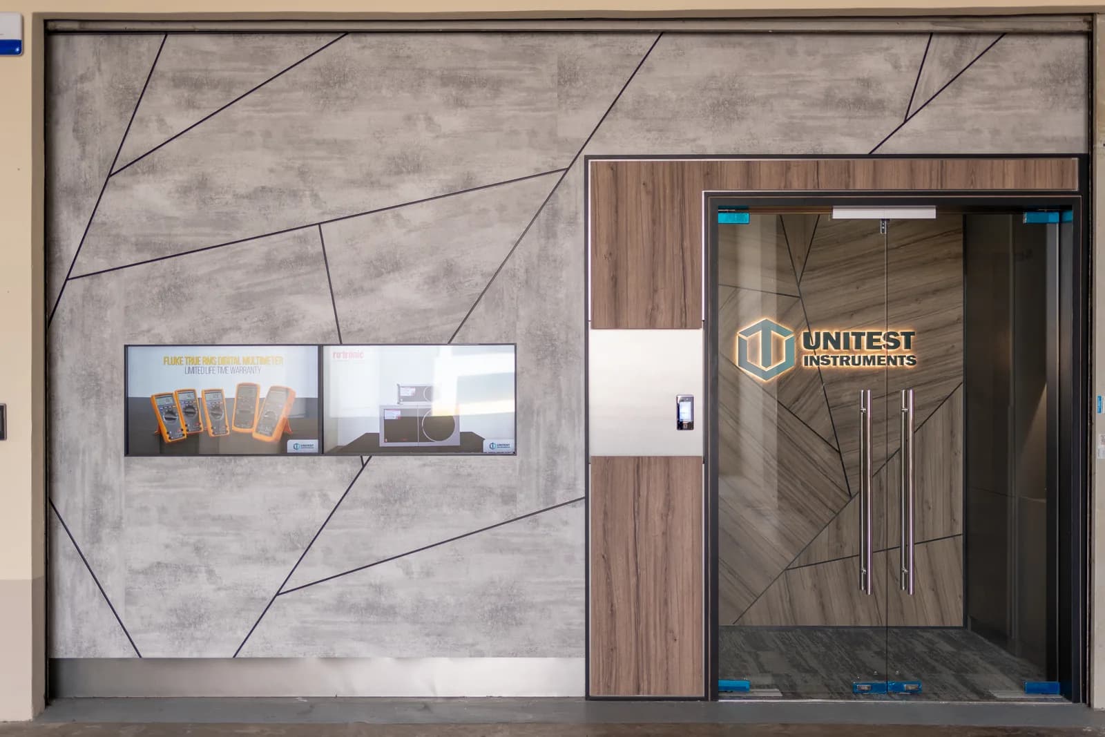 Unitest Instruments storefront entrance with the gold logo etched on glass doors and a wall display of Fluke instruments