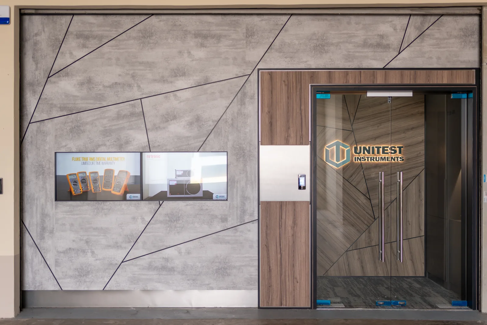 Unitest Instruments storefront entrance with the gold logo etched on glass doors and a wall display of Fluke instruments